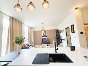 Una cocina moderna con una isla central, iluminación colgante y una zona de estar con sofá y sillas.