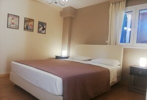A bedroom with a bed, two bedside tables, a window with curtains, and three posters on the wall. - One Bedroom Apartment with Private Patio - Suli Residences (Kefalonia)