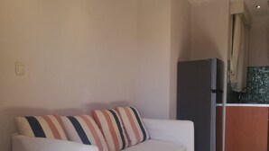 Ein weißes Sofa mit gestreiften Kissen in einem Raum mit Fliesenboden und einer Küche im Hintergrund.