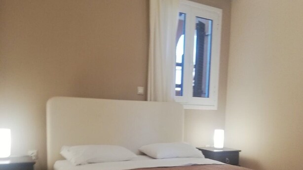 Ein Schlafzimmer mit Bett, Nachttischen, einem Fenster mit Vorhängen und einer Kristallleuchter.