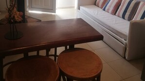 Ein Wohnzimmer mit einer Couch, einem Esstisch mit zwei Hocker, einer Tür und einem kleinen Tisch mit einer Vase.