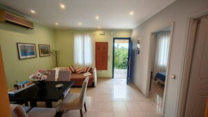 Quarto de hotel com área de refeições, sofá, guarda-roupa de madeira e vista para o exterior.