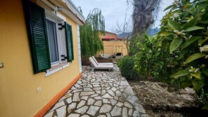 Um edifício amarelo com persianas verdes, um caminho de pedra, uma espreguiçadeira e uma rede.