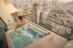 Piscina infinita en la azotea con vistas a la ciudad, barandilla de vidrio y una mesa con velas y aperitivos.