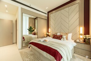 A modern bedroom with a large bed, a mirror, and a nightstand with a vase of flowers. - Binghatti Royale • Elite 1BR Suite - Top Area (Dubai)