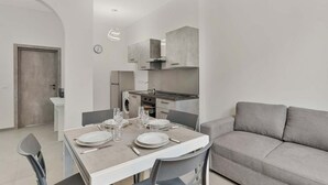 Una cocina moderna con armarios grises, una mesa de comedor con platos y vasos, y un sofá gris en la sala de estar.