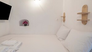 A hotel room with a bed, a wall-mounted TV, a small flower vase, and a wooden shelf.