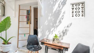 Een klein terras met een houten tafel en stoelen, een plant in pot, en een ladder die tegen een muur staat.