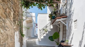 A narrow street with white buildings, a stone wall, and a small table with chairs.