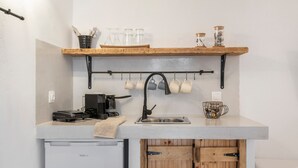 Eine kompakte Küche mit integriertem Geschirrspüler, einer Kaffeemaschine und einem Wandregal für Tassen.