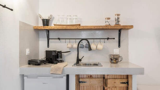 A compact kitchen with a built-in dishwasher, a coffee maker, and a hanging mug rack.