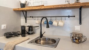 A kitchen with a stainless steel sink, a coffee maker, a kettle, and a mug rack.