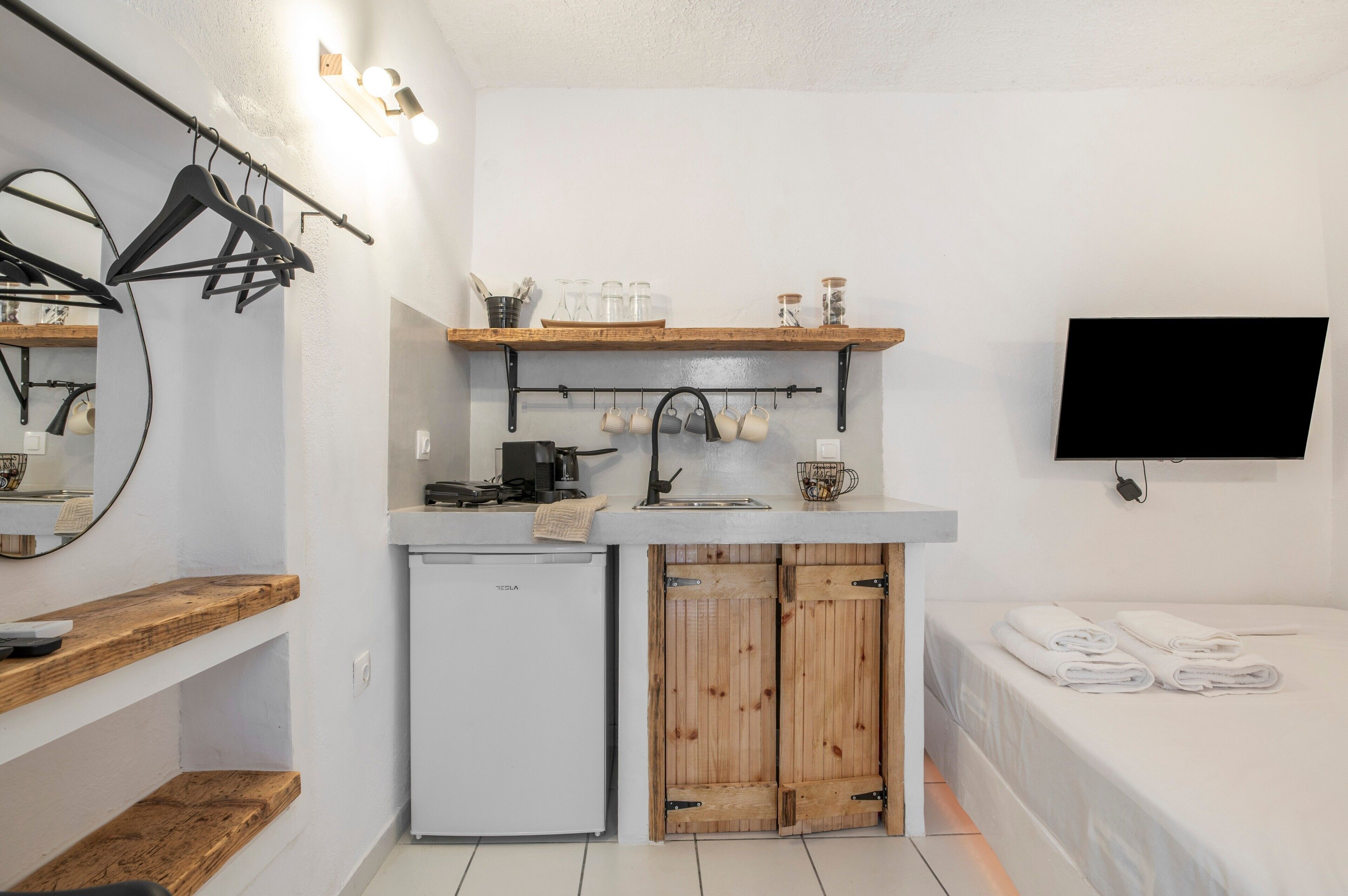 Une petite cuisine équipée, avec un réfrigérateur intégré, des placards en bois et un téléviseur à écran plat fixé au mur.
