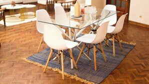 Un espace repas avec une table en verre entourée de chaises blanches, un tapis à motifs et un plancher en bois.