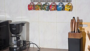 Une cuisine équipée d’une machine à café, d’un bloc à couteaux et d’un ensemble de tasses colorées accrochées au mur.