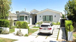Uma casa moderna de dois andares com fachada branca, entrada por meio de calçada e um carro branco estacionado.