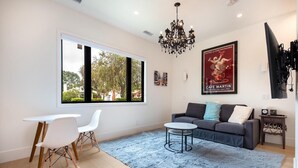 Uma sala de estar moderna com uma janela grande, um sofá cinza, uma mesa branca e um lustre.
