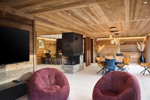 A modern interior with a wooden ceiling, a stone fireplace, and a dining area with chairs and a table. - Chalet Phoenix - 14 guests - Spa & Hammam, Gérardmer (Gérardmer)
