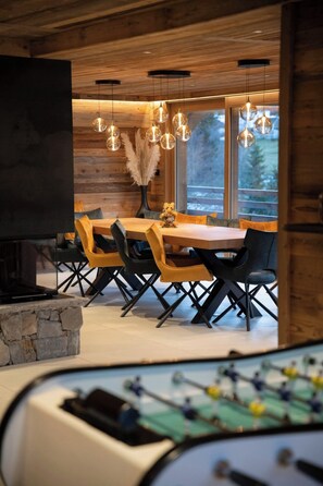 A modern dining area with a wooden table and chairs, a stone fireplace, and hanging spherical light fixtures. - Chalet Phoenix - 14 guests - Spa & Hammam, Gérardmer (Gérardmer)