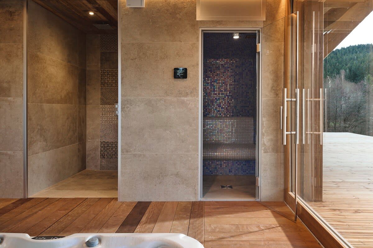 Un área de spa con un jacuzzi, ducha a nivel de piso y sauna con paredes de vidrio.