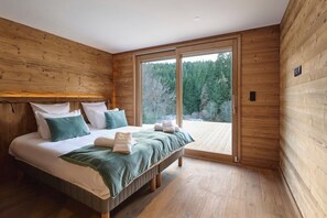 A bedroom with a large bed, wooden walls, and a sliding glass door leading to a balcony. - Chalet Phoenix - 14 guests - Spa & Hammam, Gérardmer (Gérardmer)