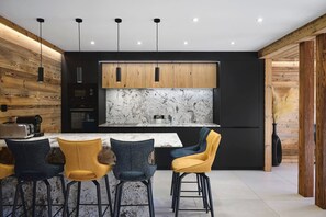 A modern kitchen with a marble backsplash, wooden cabinets, and a central island with bar stools. - Chalet Phoenix - 14 guests - Spa & Hammam, Gérardmer (Gérardmer)