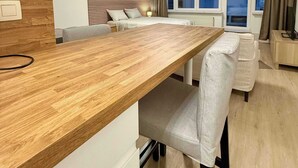A modern hotel room with a wooden dining table, a sofa, a bed with a headboard, and a large window with curtains. - Studio moderne au coeur du quartier Saint Adalbert (Liège)