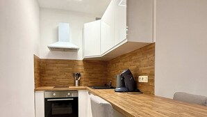 A modern kitchen with white cabinets, a wooden countertop, a built-in oven, and a coffee machine. - Studio moderne au coeur du quartier Saint Adalbert (Liège)