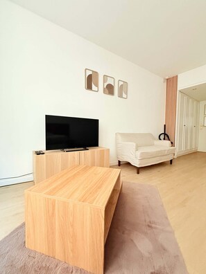 A modern living room with a flat-screen TV on a wooden stand, a beige sofa, and a coffee table. - Bright Modern Studio in the Heart of Saint-Adalbert (Liège)