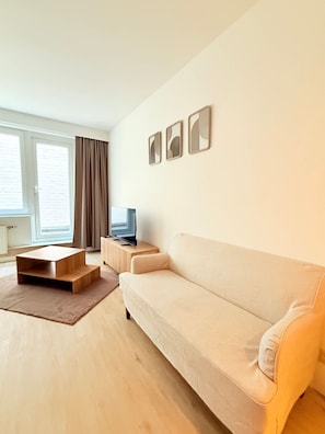 Ein modernes Wohnzimmer mit einer Couch, einem Couchtisch, einem Fernseher auf einem Schrank und einem Fenster mit Vorhängen.