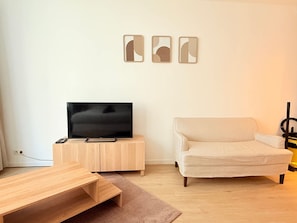 Ein Wohnzimmer mit Flachbildfernseher auf Holzständer, einem beigen Sofa und einem Couchtisch.