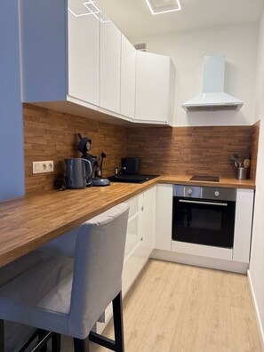 A modern kitchen with white cabinets, a wooden countertop, a built-in oven, and a coffee machine. - Bright Modern Studio in the Heart of Saint-Adalbert (Liège)