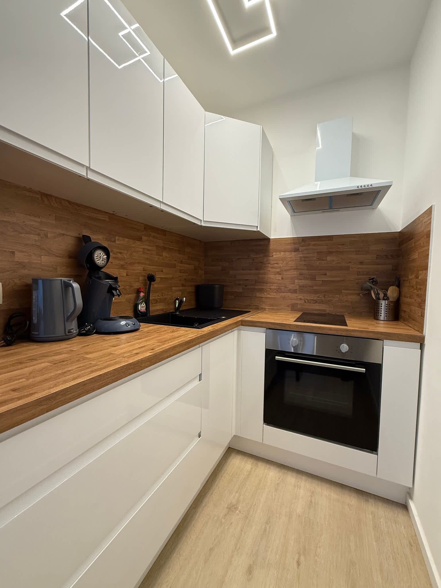 Une cuisine moderne avec des meubles blancs, un plan de travail en bois, un four encastré et une machine à café.