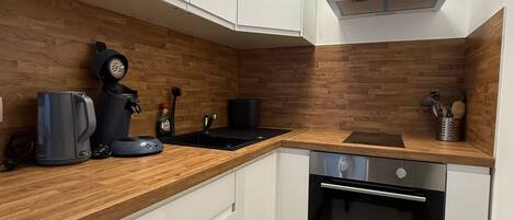 A modern kitchen with white cabinets, a wooden countertop, a built-in oven, and a coffee maker.
