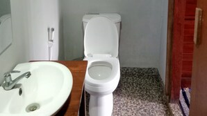 Un bagno con un WC bianco, un mobile bagno in legno con un lavandino bianco e un pavimento piastrellato.