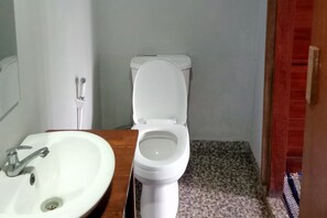 A bathroom with a white toilet, a wooden vanity with a white sink, and a tiled floor. - TwoSpaces Living at Welirang Resort Syariah (Pacet)