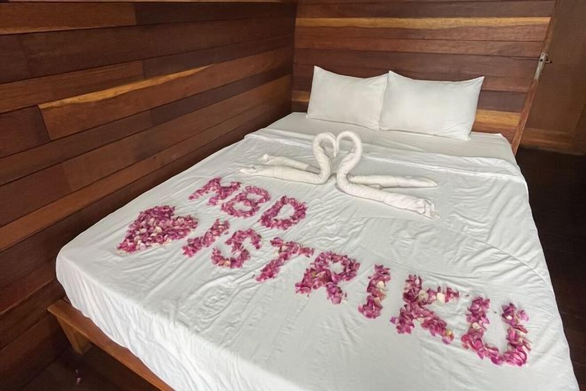 A bed with a white sheet, a wooden headboard, and a message made of flowers spelling 'LOVE STRIKES'.