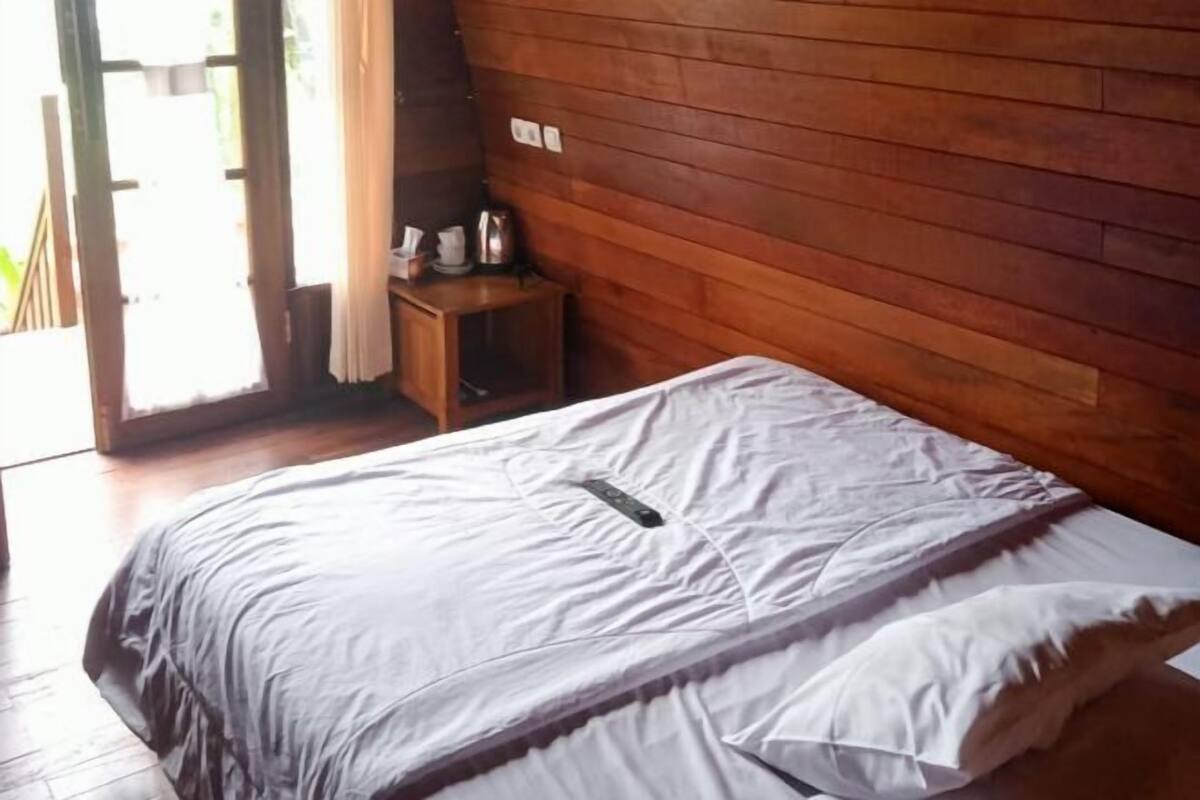 Une pièce aux murs lambrés, avec un lit, une petite table et une bouilloire, et une porte donnant sur l’extérieur.