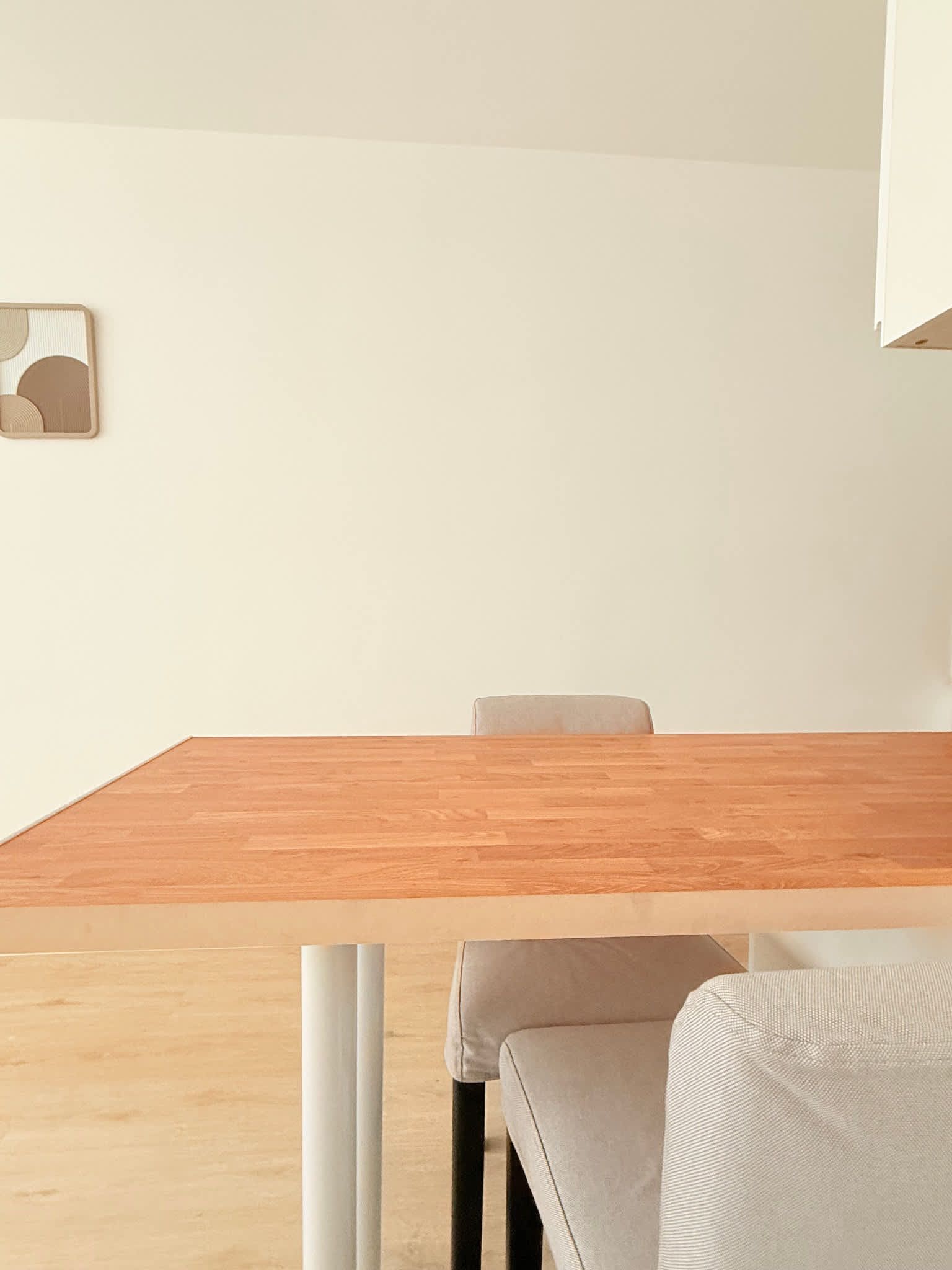 Een minimalistische kamer met een houten tafel, een grijze stoel en een witte muur.
