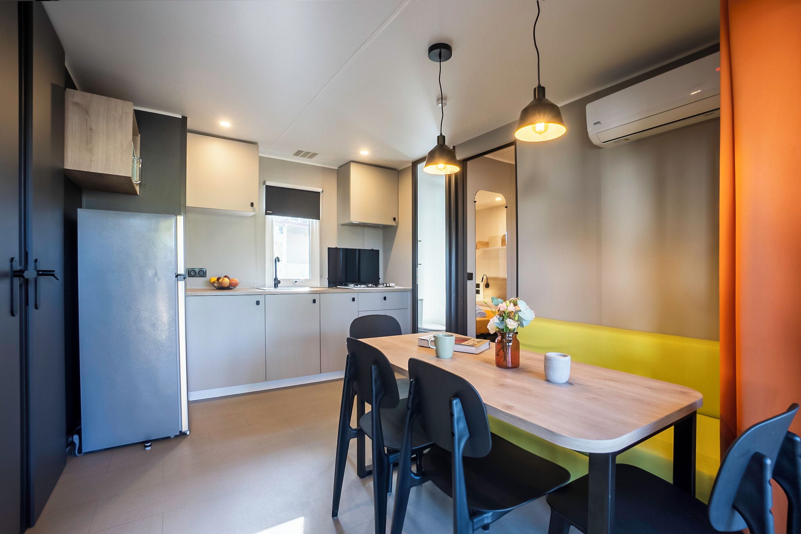 A modern kitchen with a dining area, featuring a wooden table, black chairs, and pendant lighting.