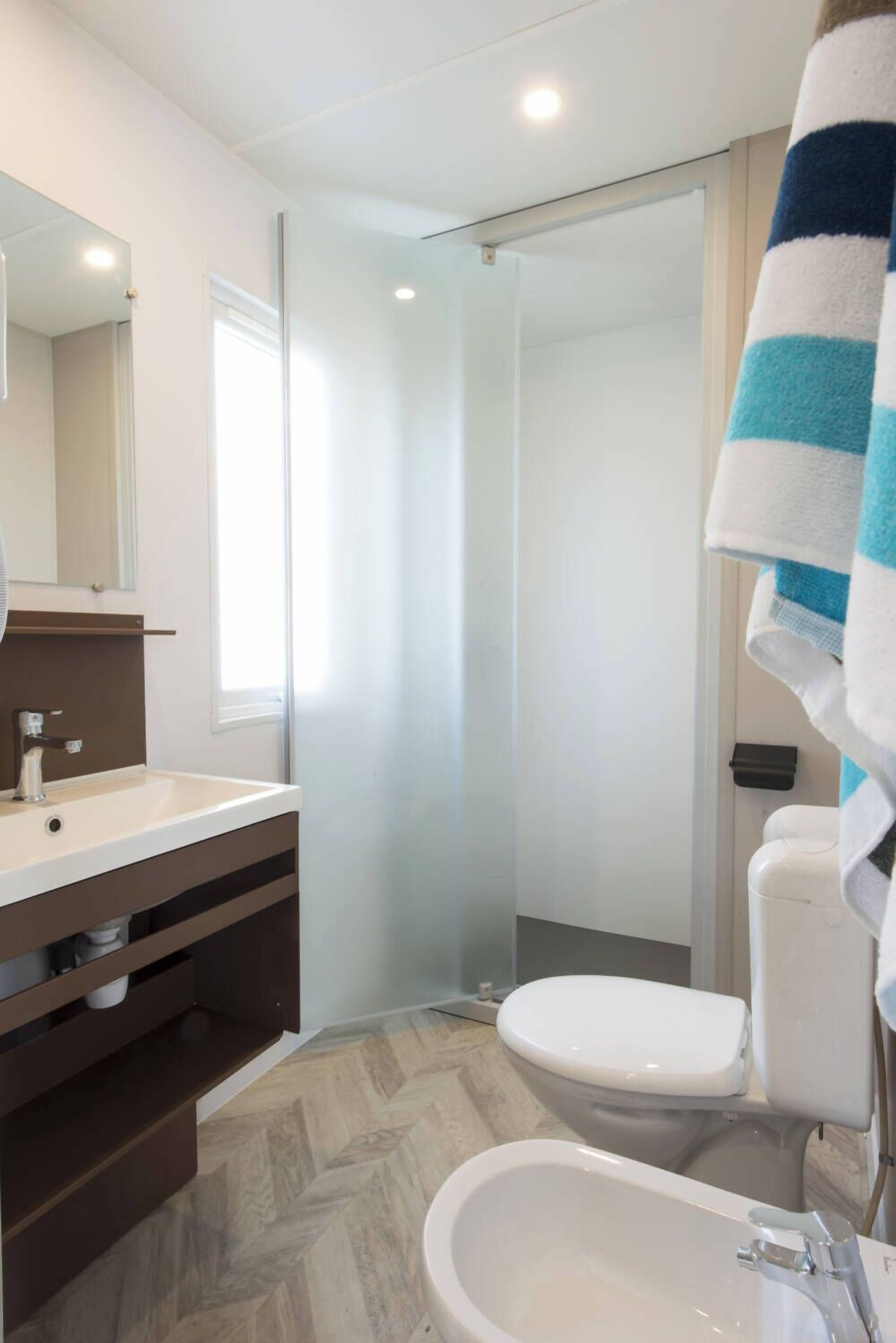 A modern bathroom with a white sink, dark wooden vanity, a glass shower enclosure, and a white toilet.