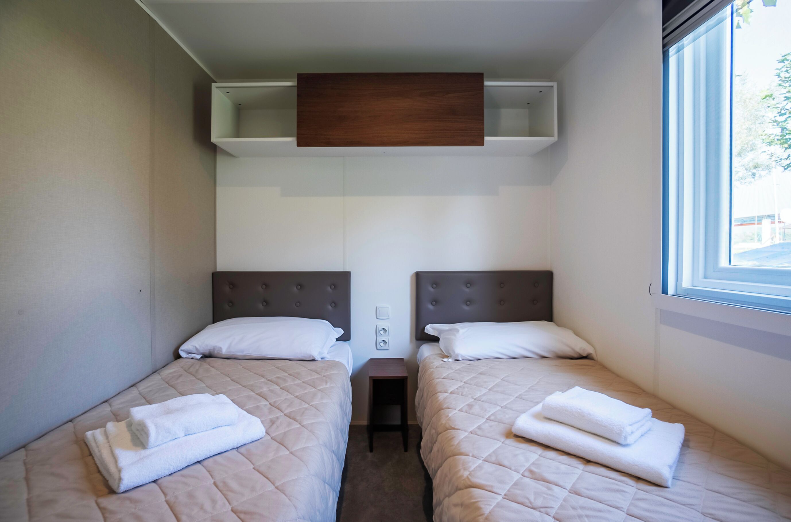 Une chambre d’hôtel avec deux lits, chacun doté d’une tête de lit, d’une petite table et d’une fenêtre.