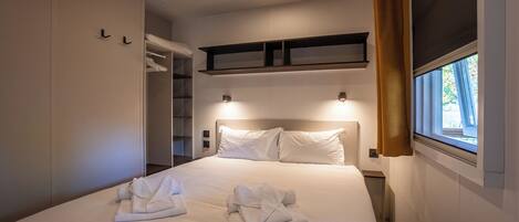 A hotel room with a large bed, a wardrobe, a shelf above the bed, and a window with curtains.