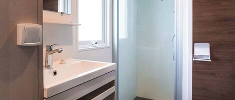 Une salle de bain moderne avec un lavabo blanc, un miroir et des toilettes. Elle comprend un espace de douche vitré et un panneau mural en bois.