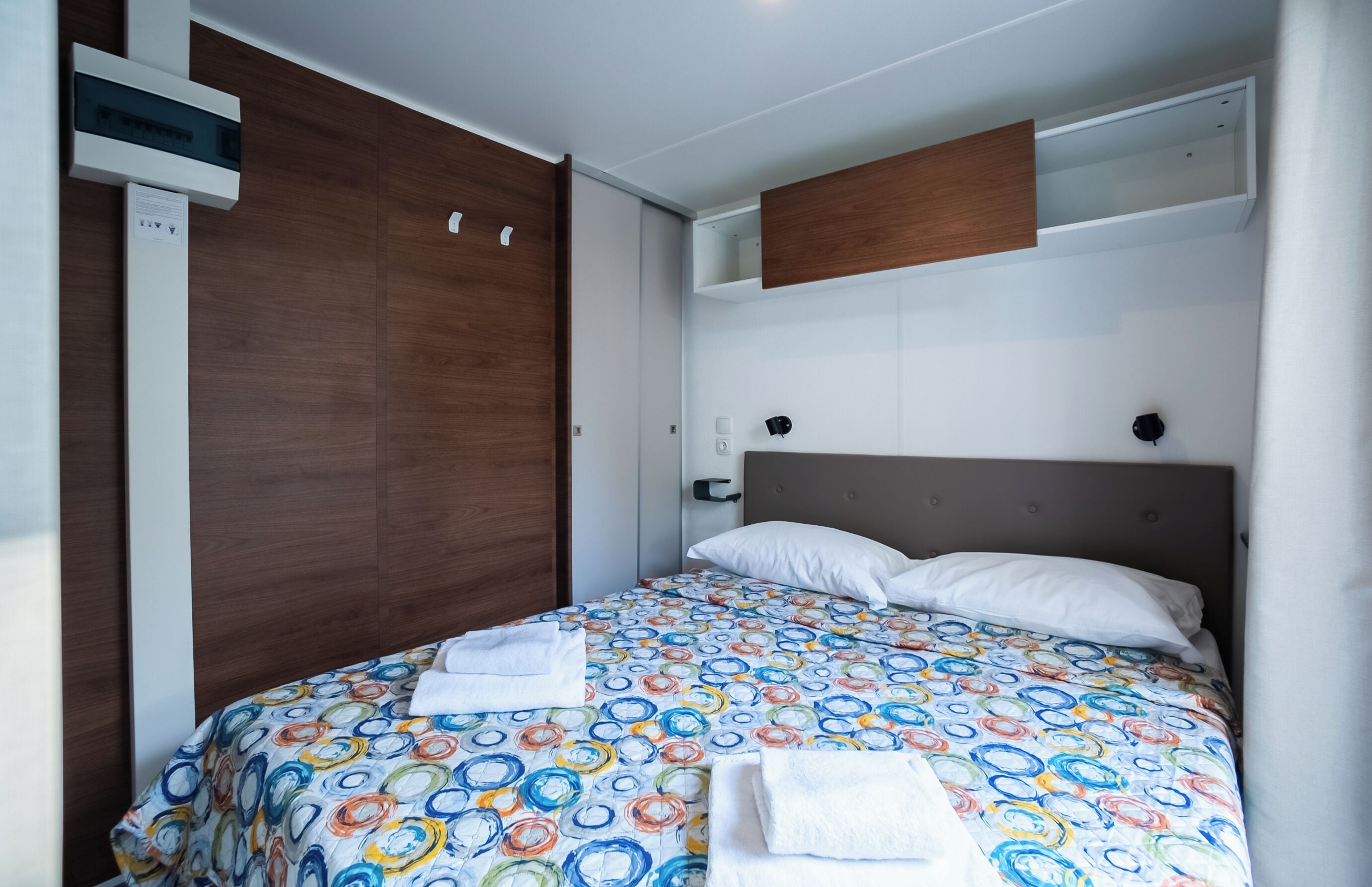 Une chambre à coucher comprenant un lit, une armoire en bois, une étagère intégrée et un climatiseur fixé au mur.