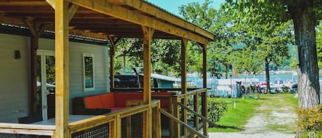 En træterrasse med et overdækket opholdsområde, et indhegnet område og en sti, der fører til en parkeringsplads med både.
