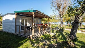 A small cabin with a porch, a covered seating area, and a view of a lake. - Lido Verbano Camping Village  (Castelletto Sopra Ticino)