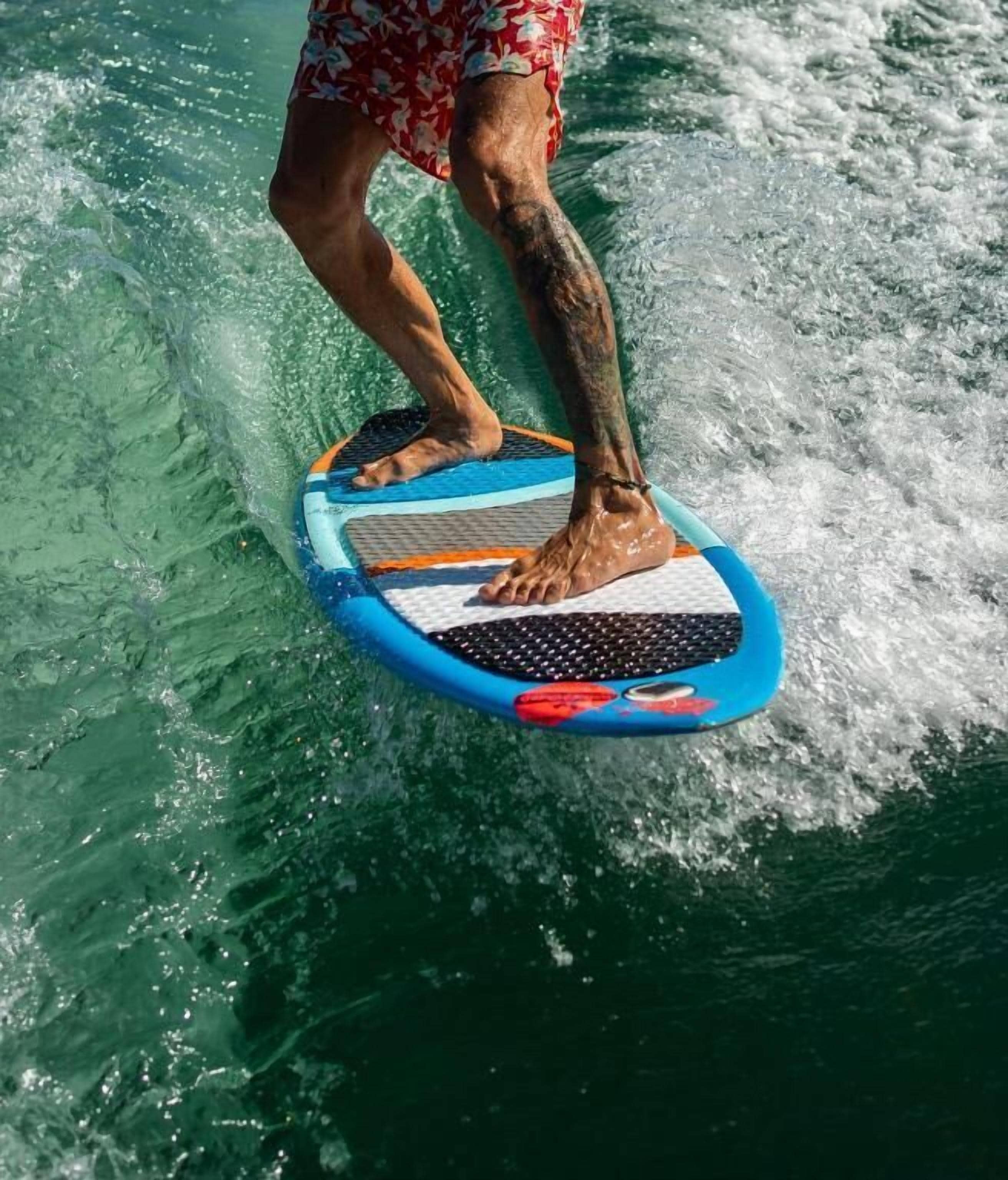 Eine Person surft auf einem blau-orangenen Surfbrett in klarem Wasser.