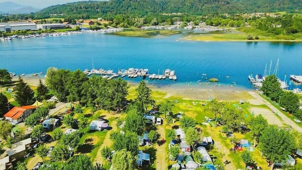 An aerial view of a lakeside area with boats docked, a marina, and a campground with tents and RVs. - Lido Verbano Camping Village  (Castelletto Sopra Ticino)