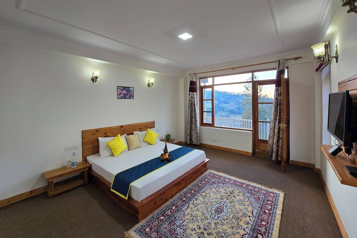 Une chambre dotée d’un grand lit, de tables de chevet, d’un téléviseur et offrant une vue sur un paysage montagneux grâce à une grande fenêtre.